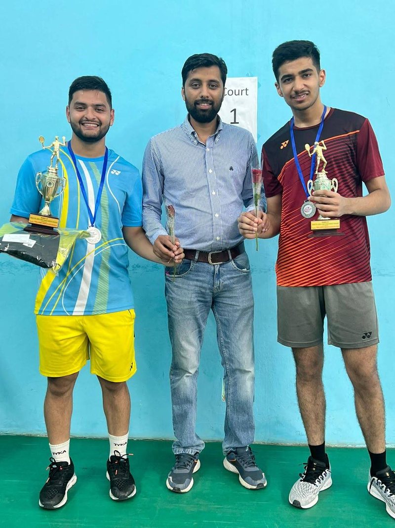 Shikhar Rallan and Shubham Bhatt holding trophies either side of Coach Suresh Kumar on court